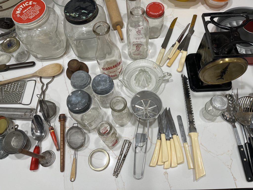 Vintage kitchen utensils, glass jars, milk bottles and household items being sorted for an estate sale